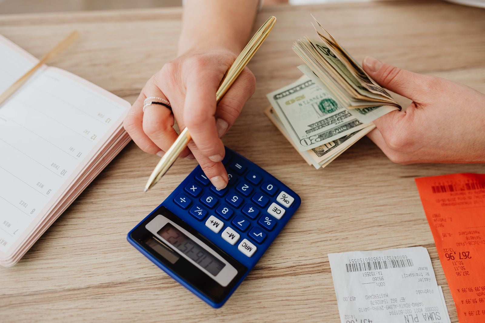 Hands using a calculator beside cash and budget notes, illustrating the cost of PMP certification.