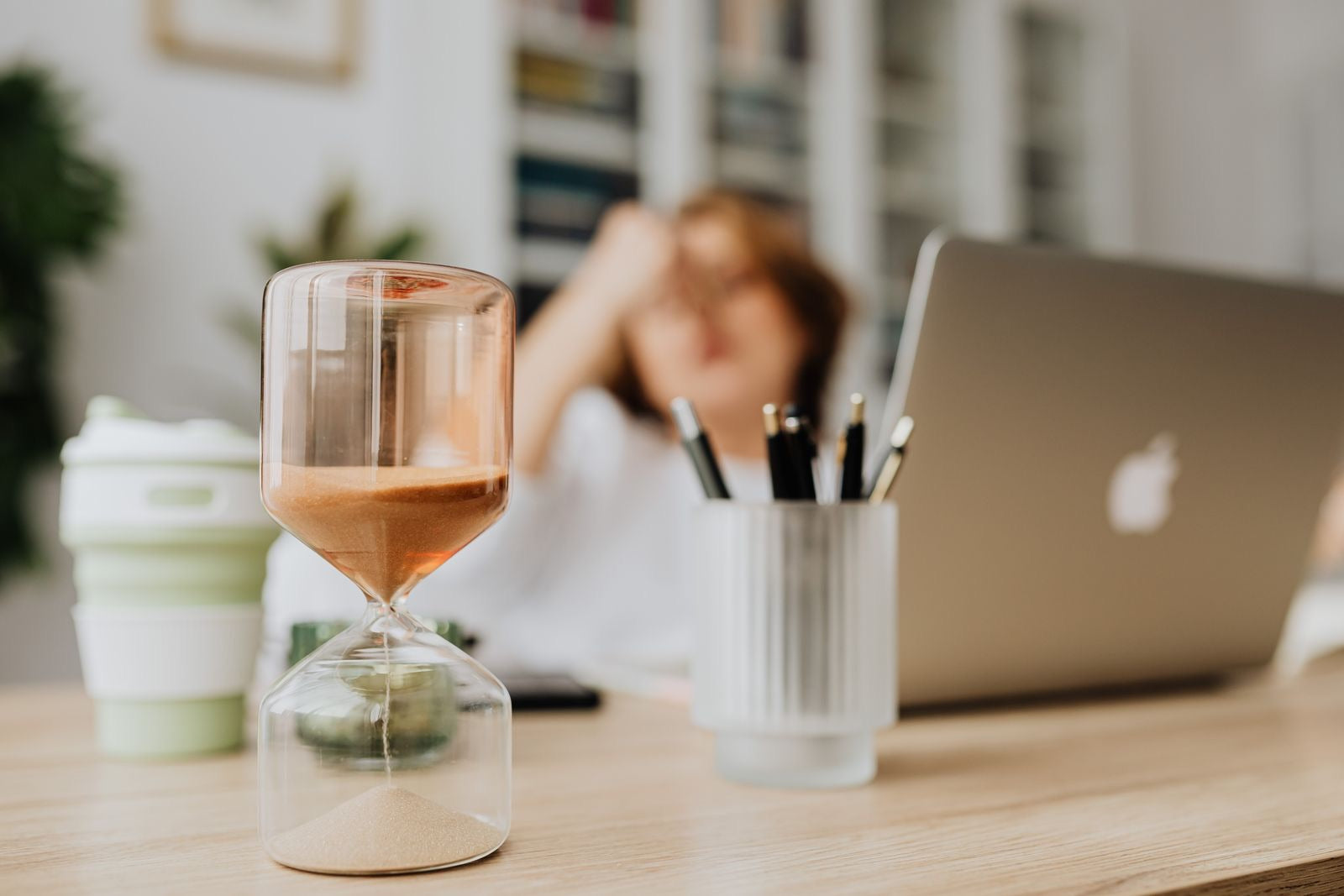 An hourglass on a desk beside a laptop, representing how long to study for the PMP exam.